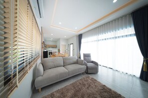 En moderne stue med sofa, lænestol og et stort vindue med gardiner.