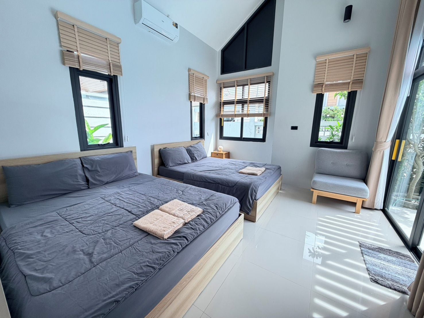 Une chambre moderne avec deux lits, un canapé et de grandes fenêtres équipées de stores.