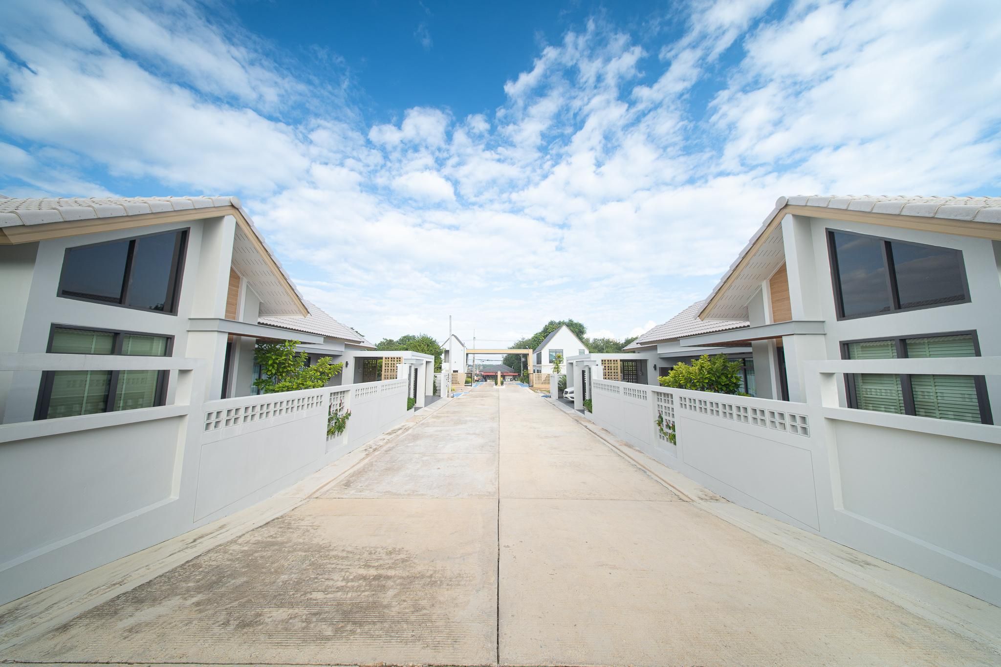 A straight pathway leading to a building with a flat roof and large windows, flanked by white walls with a grid-like pattern.