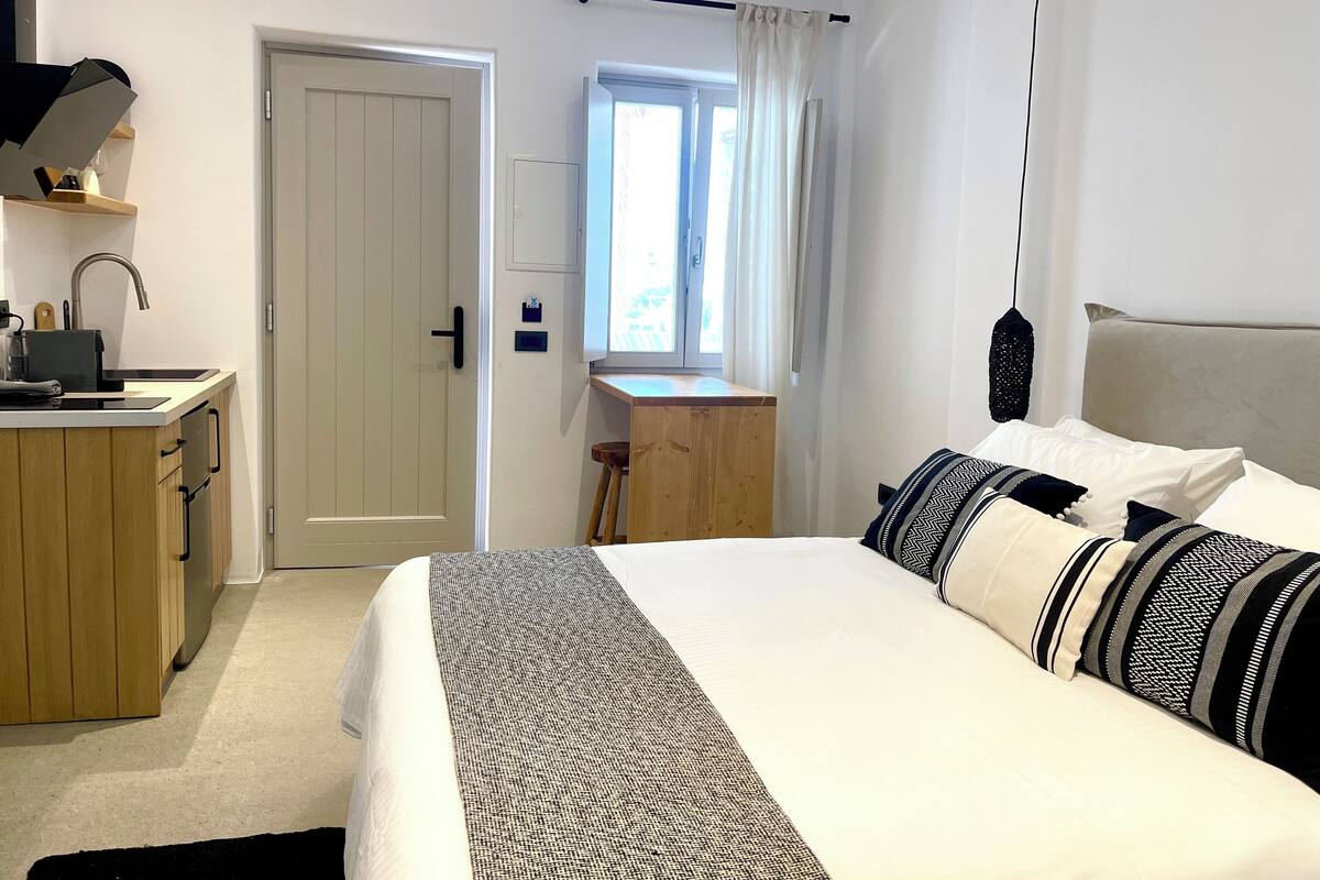 A hotel room with a bed, a desk, a kitchenette, and a window with curtains.