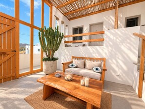 A room with a wooden bench, a potted cactus, and a sofa with cushions. - Mykonos Dot Suites (Ano Mera)