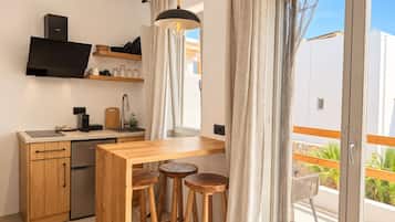 A compact kitchen with a built-in oven, a coffee machine, and a sink. There is a wooden table with stools and a hanging pendant light.