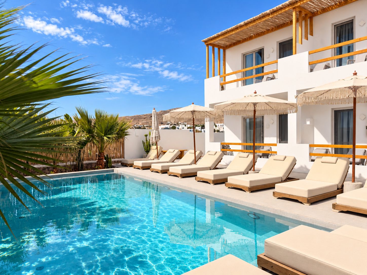 A swimming pool with lounge chairs and umbrellas, surrounded by a white building with balconies.