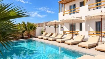A swimming pool with lounge chairs and umbrellas, surrounded by a white building with balconies.