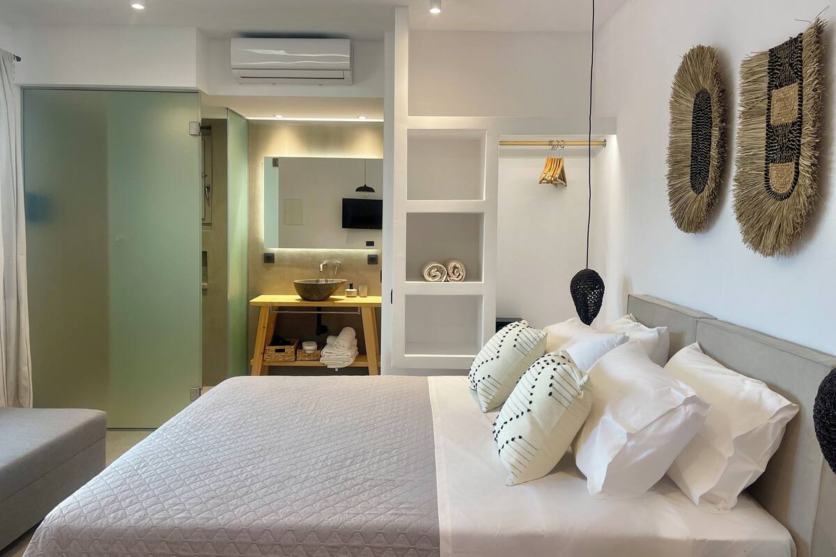 A modern bedroom with a large bed, a bedside table, a mirror, and a wall-mounted TV.