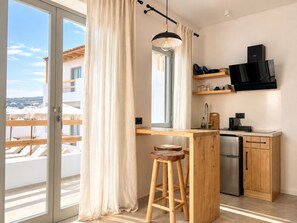 A modern kitchen with a built-in oven, wooden stools, and a large window with curtains. - Mykonos Dot Suites (Ano Mera)