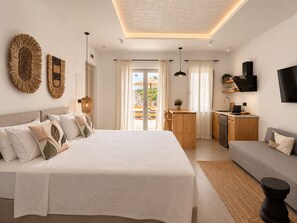 A modern bedroom with a large bed, a wooden desk, a grey sofa, and a TV mounted on the wall. - Mykonos Dot Suites (Ano Mera)