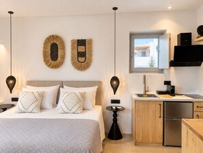A modern bedroom with a bed, bedside tables, and a nightstand. There is a kitchen area with a sink, stove, and refrigerator. - Mykonos Dot Suites (Ano Mera)