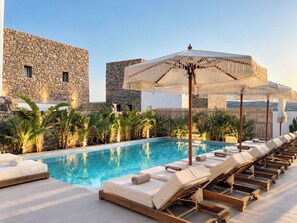 A pool area with lounge chairs and umbrellas, surrounded by stone walls and tropical plants. - Mykonos Dot Suites (Ano Mera)