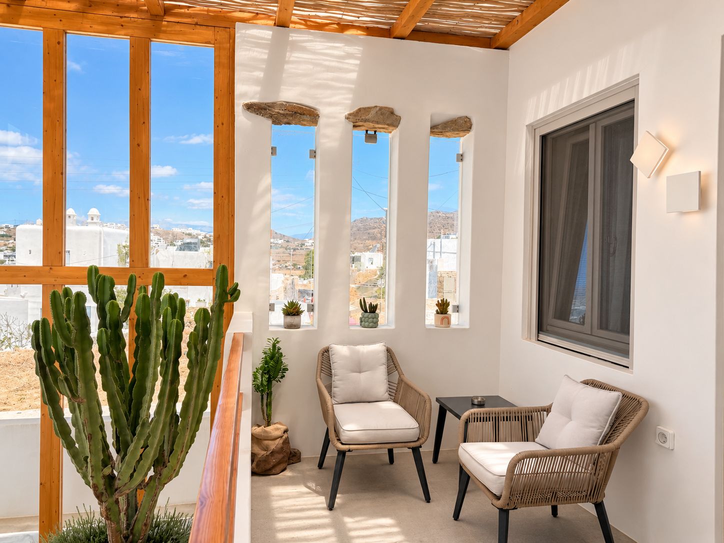 Ein Balkon mit Korbmöbeln, einer Kakteenpflanze und Blick auf eine Küstenstadt.