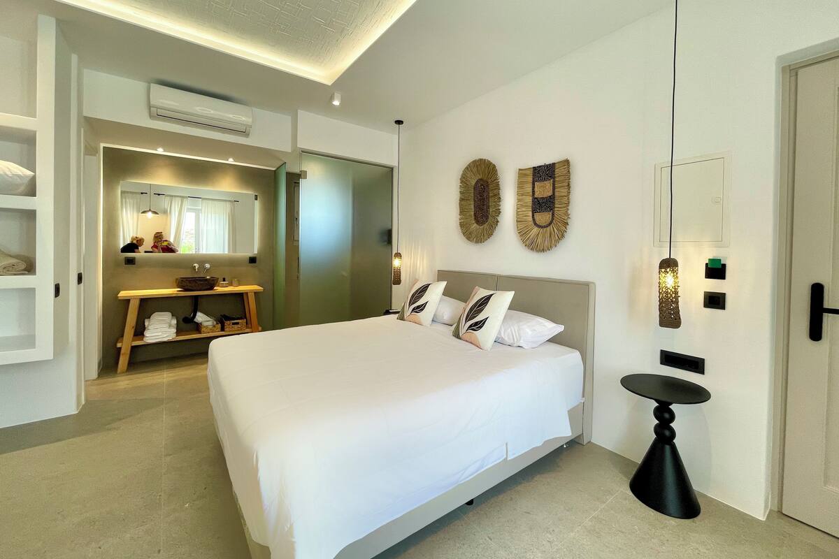 A modern hotel room with a large bed, a vanity with a mirror, and a small table.