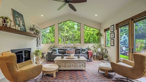 A spacious living room with a large window, a ceiling fan, a fireplace, and a sofa set. - Hot tub, Outdoor dining, BBQ Grill, Fire pit & Gym (Colorado Springs)