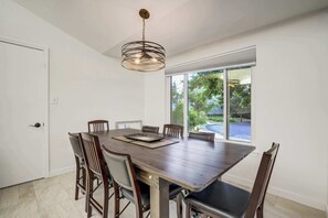 A dining area with a large table, chairs, and a hanging light fixture.