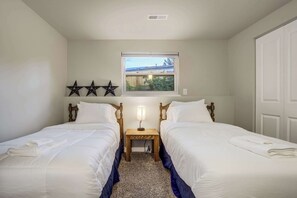 A hotel room with two beds, a small table, a lamp, and a window with a view of a fence and trees. - Fountain Mountain|Trails & Wildlife|BBQ + Fire Pit (Fountain)
