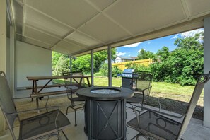 An outdoor patio area with a round table, metal chairs, a grill, and a wooden bench.