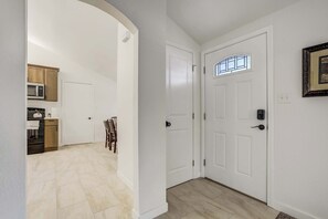 Un couloir mène à une salle à manger avec une porte blanche, une cuisine dotée de meubles en bois et un tableau encadré accroché au mur.