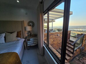 Une chambre à coucher comprenant un lit, une table de chevet, une lampe et donnant sur un balcon aménagé avec du mobilier d’extérieur.