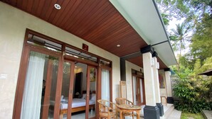 A hotel room with a wooden ceiling, large sliding glass doors, a bed, a chair, and a small table.