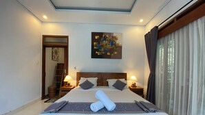 A neatly made bed with a rolled towel, two bedside tables with lamps, a painting on the wall, and a large window with curtains.