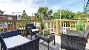 A deck with wicker furniture, a glass table, and a wooden railing.