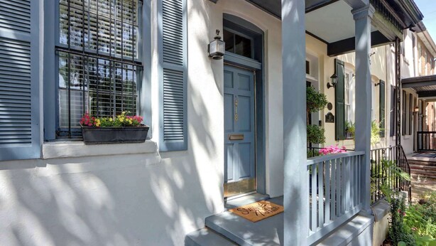 A house with a blue door, a porch with a railing, and a window with shutters.