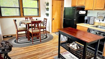 Una cocina compacta con armarios de madera, una mesa de comedor con sillas, un refrigerador negro y una cafetera.