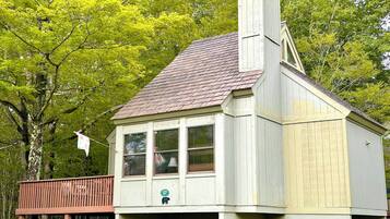 Un edificio pequeño de un piso con techo inclinado y chimenea, rodeado de árboles verdes y frondosos.