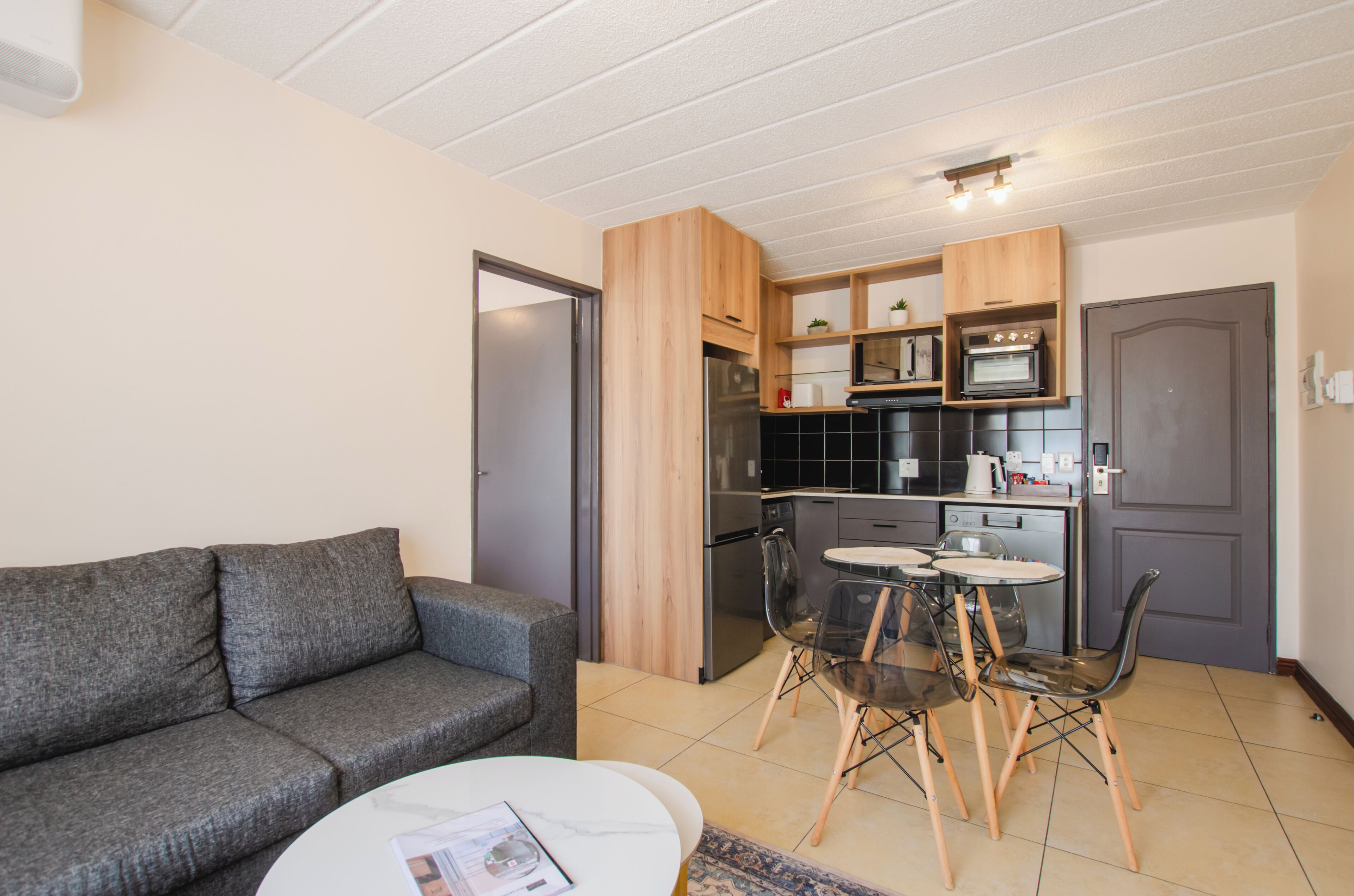 A compact living space with a kitchenette, grey sofa, dining table, and chairs.