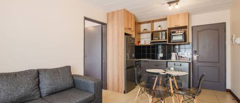 A compact living space with a kitchenette, grey sofa, dining table, and chairs.