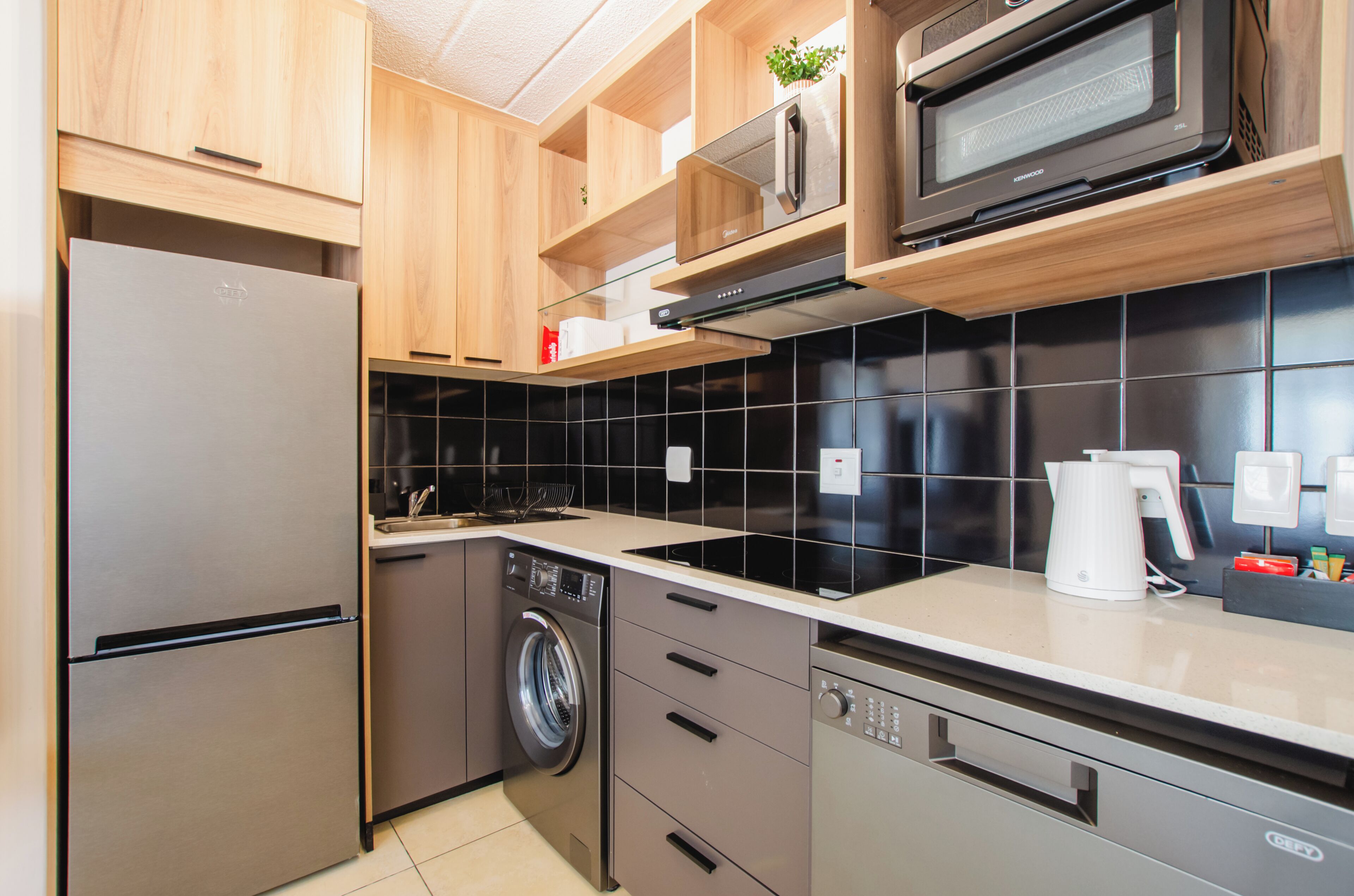 A modern kitchen with stainless steel appliances, wooden cabinets, and black tiled backsplash.