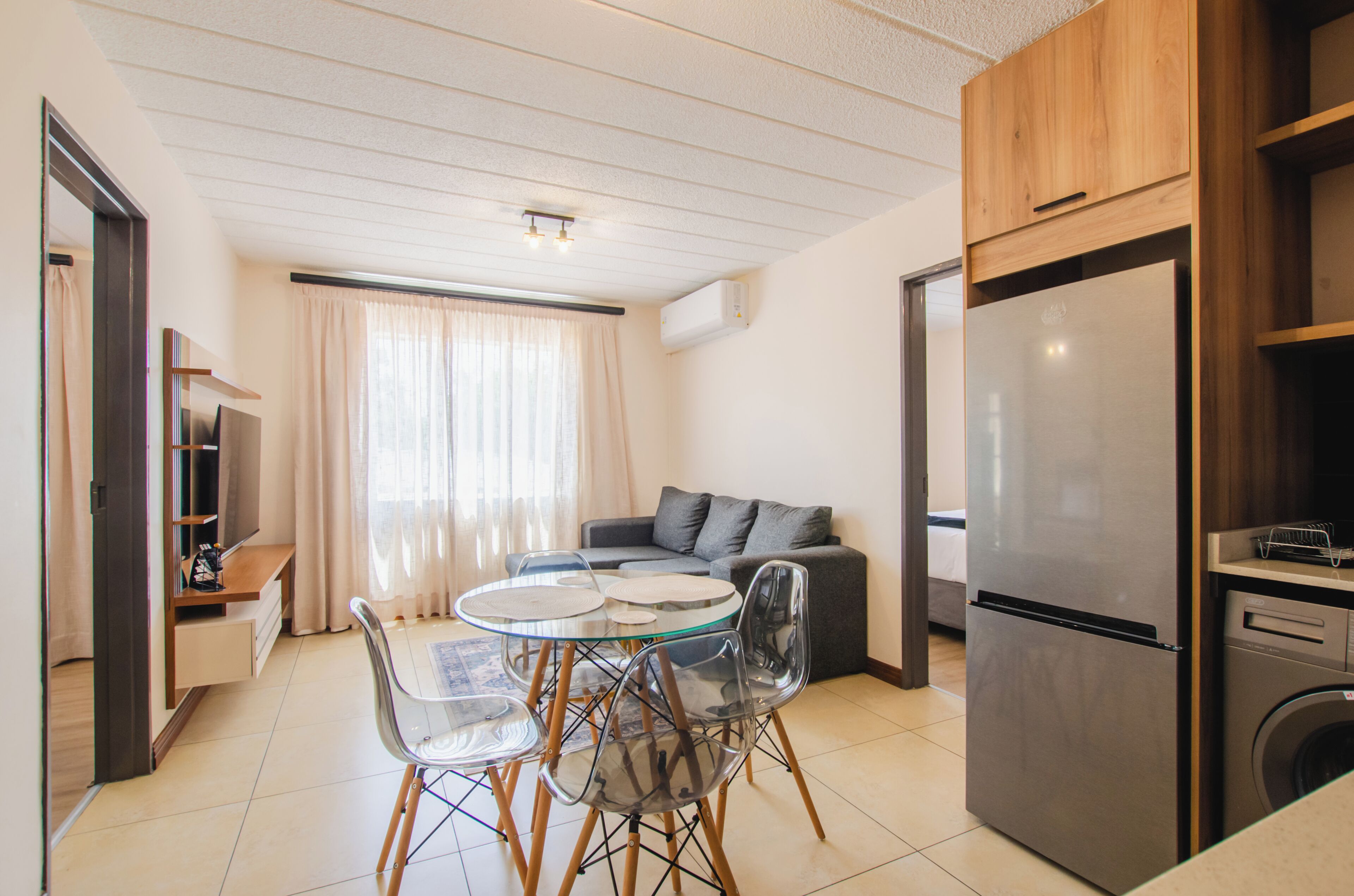A modern kitchen with a dining area, a grey sofa, and a stainless steel refrigerator.
