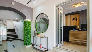 A reception area with a reception desk, a mirror, a staircase, and a green wall. - Melrose Corner (Johannesburg)