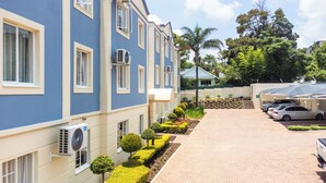 A multi-story building with a blue and beige facade, air conditioning units, a paved driveway, and parked cars. - Melrose Corner (Johannesburg)