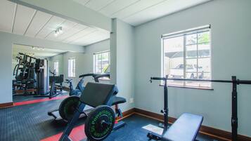 A gym with exercise equipment, a bench, and a window with a view of the outside.