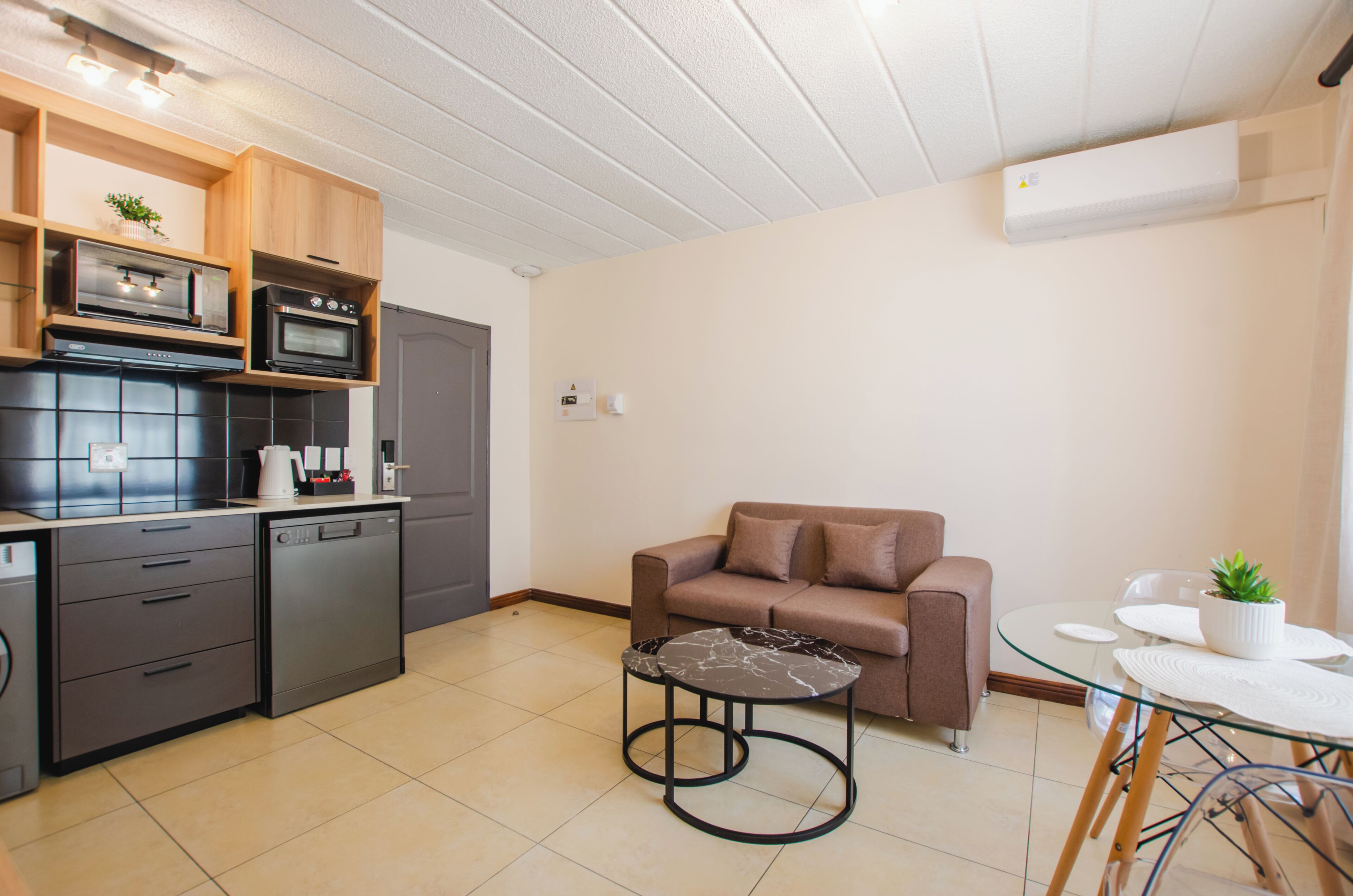 A compact kitchen with modern appliances, a sofa, and a small dining table with a potted plant.