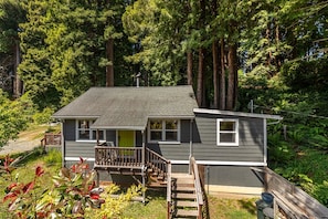 A two-story house with a front porch, surrounded by dense forest.