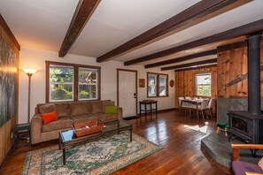 A cozy living room with a sofa, coffee table, and rug, a dining area with a table and chairs, and a wood-burning stove.