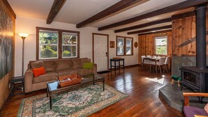 Ein gemütliches Wohnzimmer mit Sofa, Couchtisch und Teppich, ein Essbereich mit Tisch und Stühlen sowie ein Kaminofen.