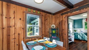 Ein Esszimmer mit Holztisch, gedeckt für vier Personen, einem Fenster und Blick zur Küche.