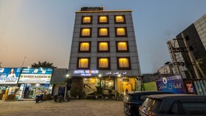 A hotel with multiple floors, a signboard for 'Hotel NexHub Palace', and several parked cars in front. - Nexhub Palace (Gurugram)