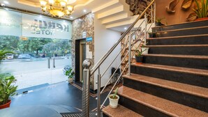 A hotel lobby with a staircase, a chandelier, and potted plants. - Nexhub Palace (Gurugram)