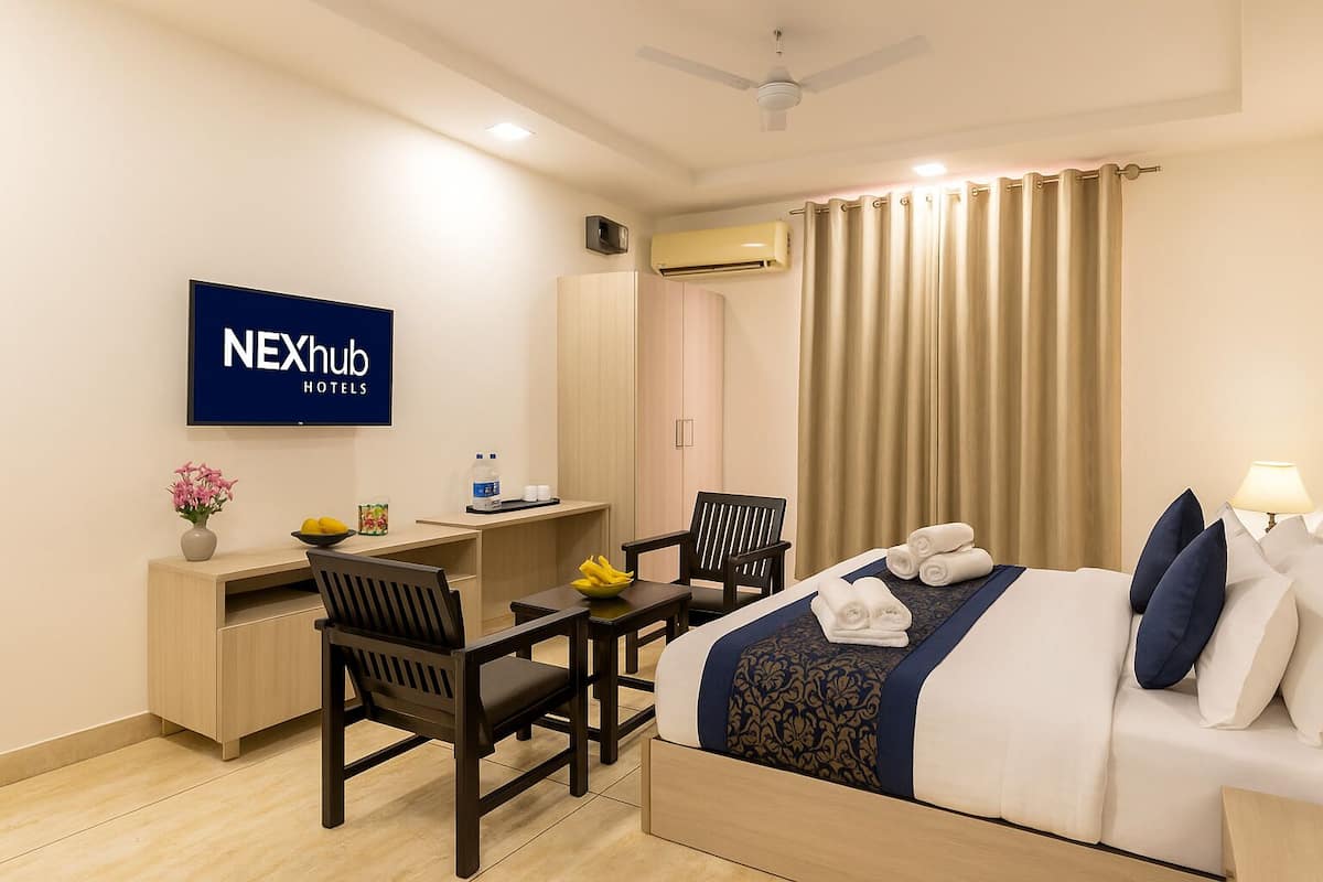 Una habitación de hotel con cama, escritorio, sillas, televisor y aire acondicionado.