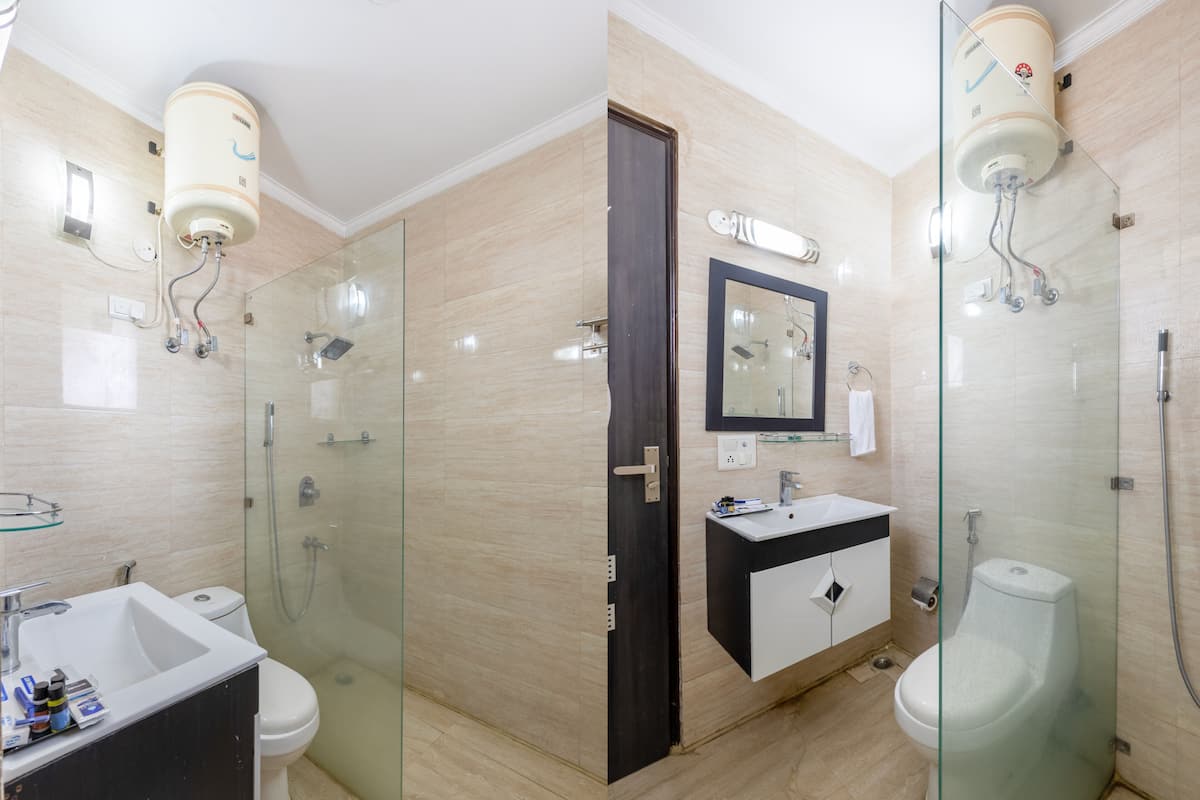 Un baño moderno con ducha envuelta en vidrio, un lavabo blanco y un mueble de tocador negro.