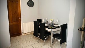 Un coin repas avec une table noire, quatre chaises noires, un radiateur blanc et une porte en bois.