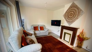 Un salon comprenant un canapé, un petit divan, une cheminée et un téléviseur fixé au mur.