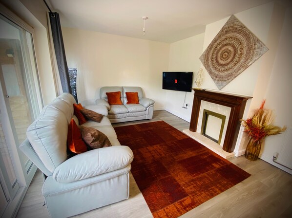 Un salon comprenant un canapé, un petit divan, une cheminée et un téléviseur fixé au mur.