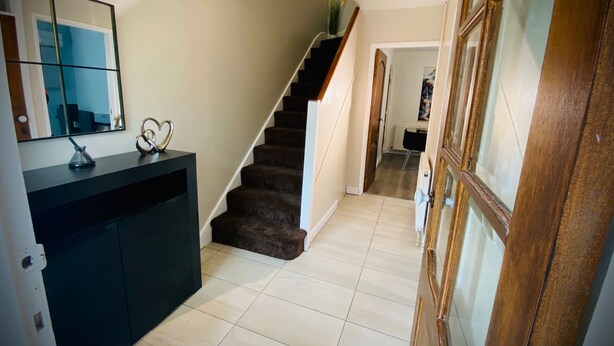 Un escalier menant à un deuxième étage, une console noire avec un miroir et une porte à panneaux de verre.