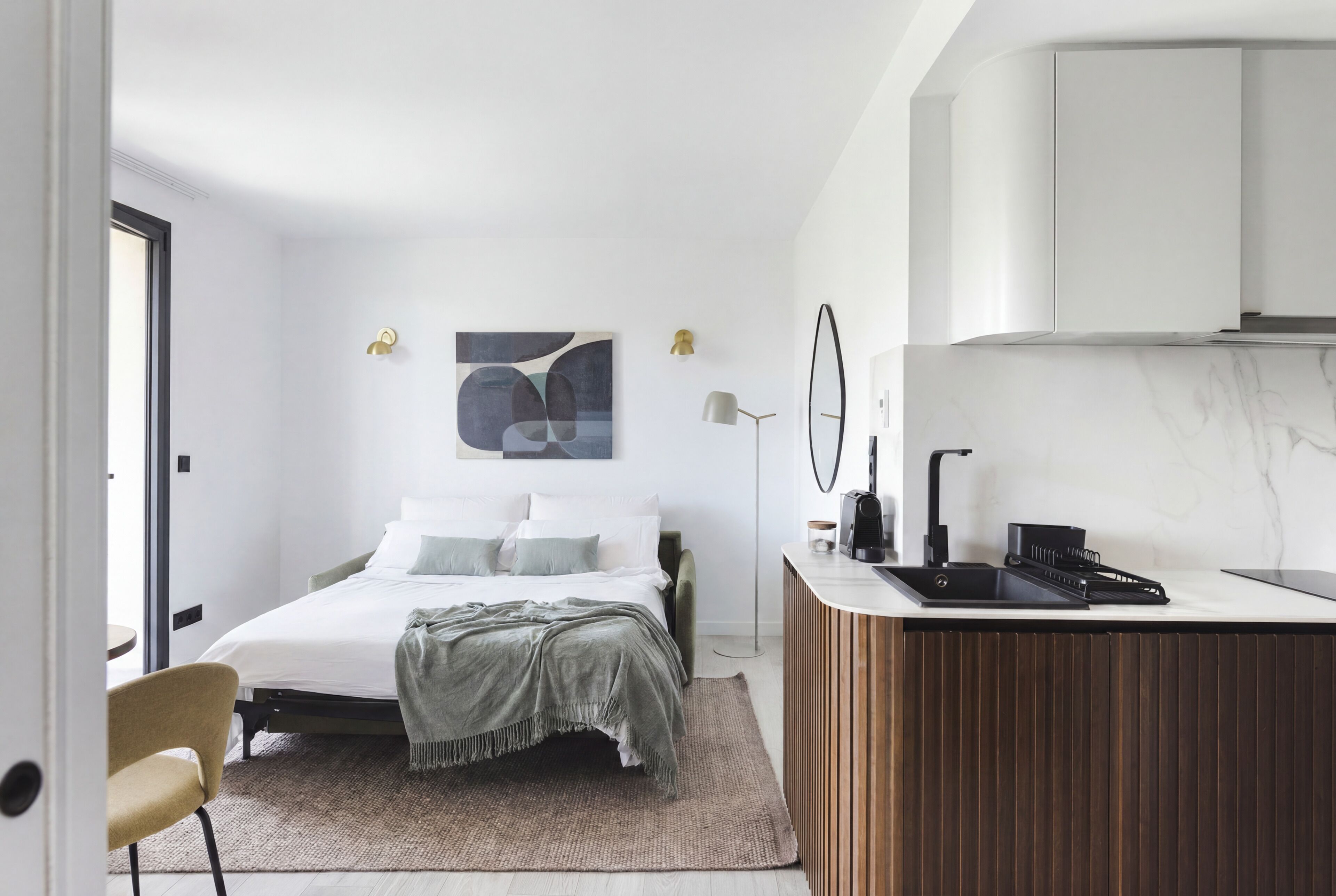 Un dormitorio con cama, mesita de noche, lámpara y vista a la cocina.