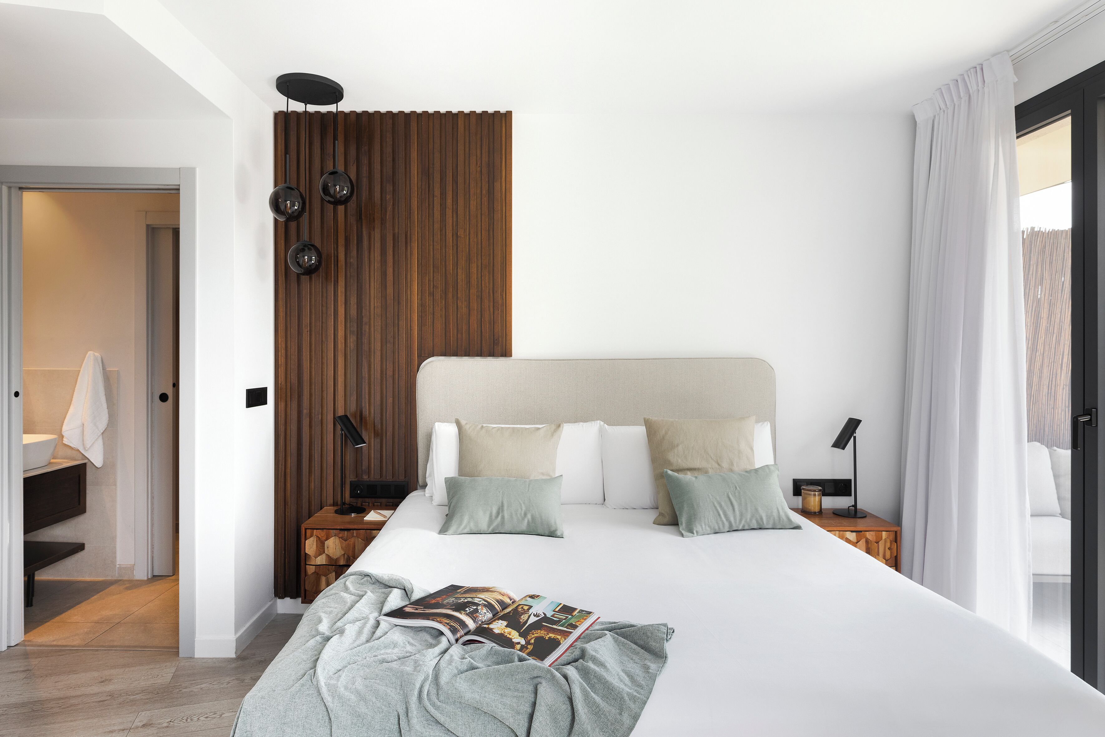 Moderni hotellihuone, jossa on suuri sänky, puupanelilla verhoiltu seinä ja näkymä parvekkeelle.