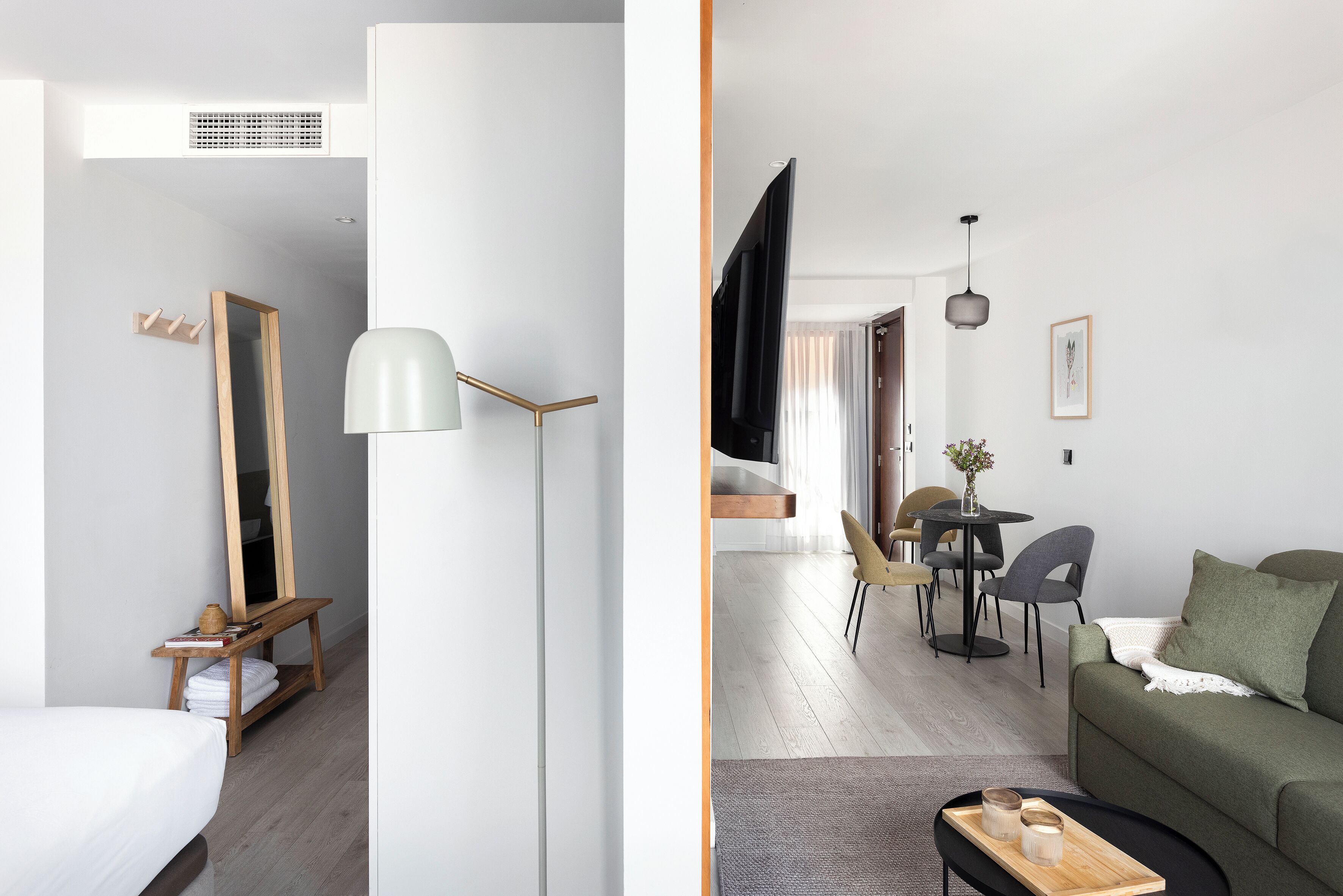 A modern hotel room with a bed, a wooden bedside table, a mirror, and a lamp.